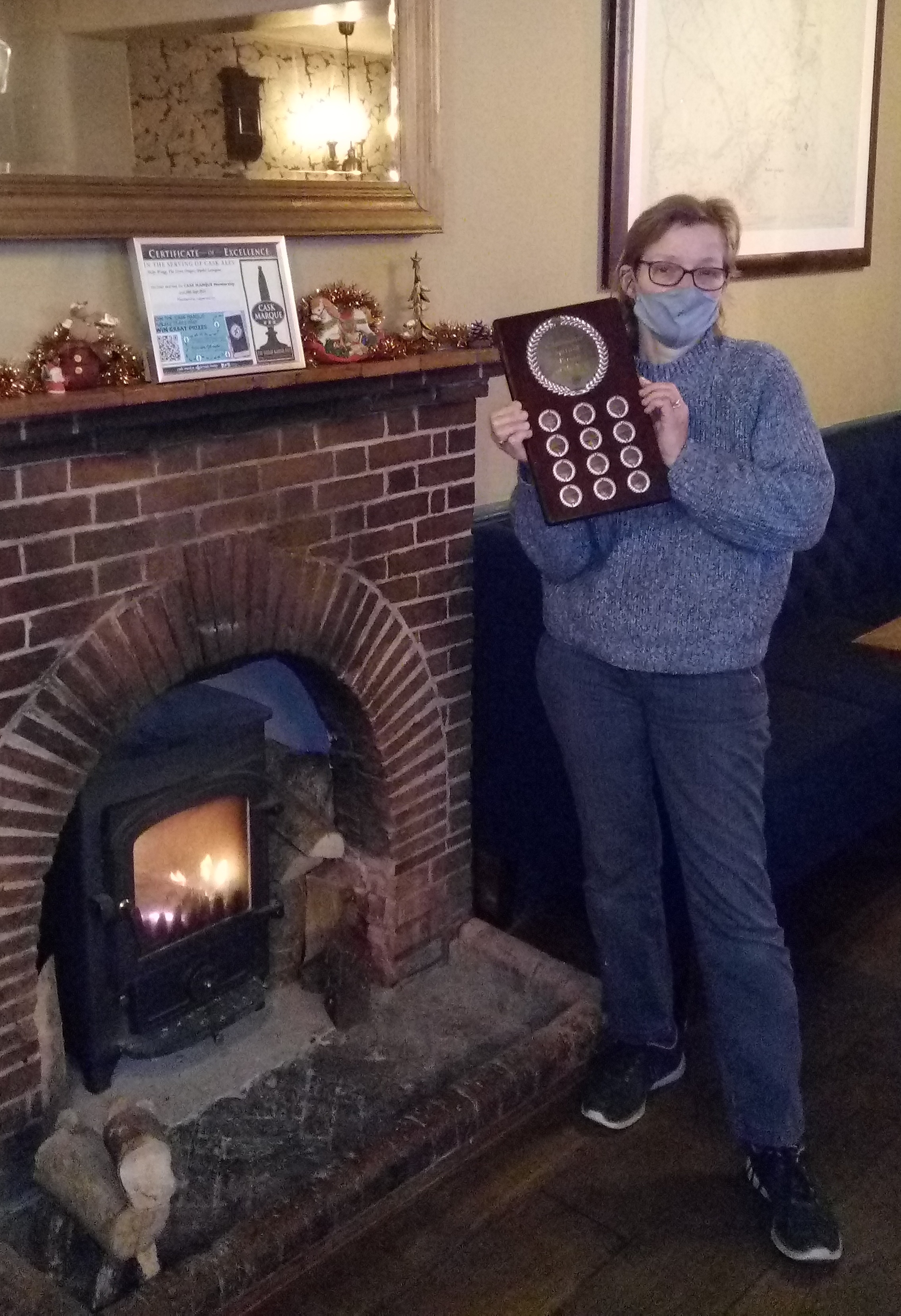 Image of Nicky holding an award shield in front of fireplace